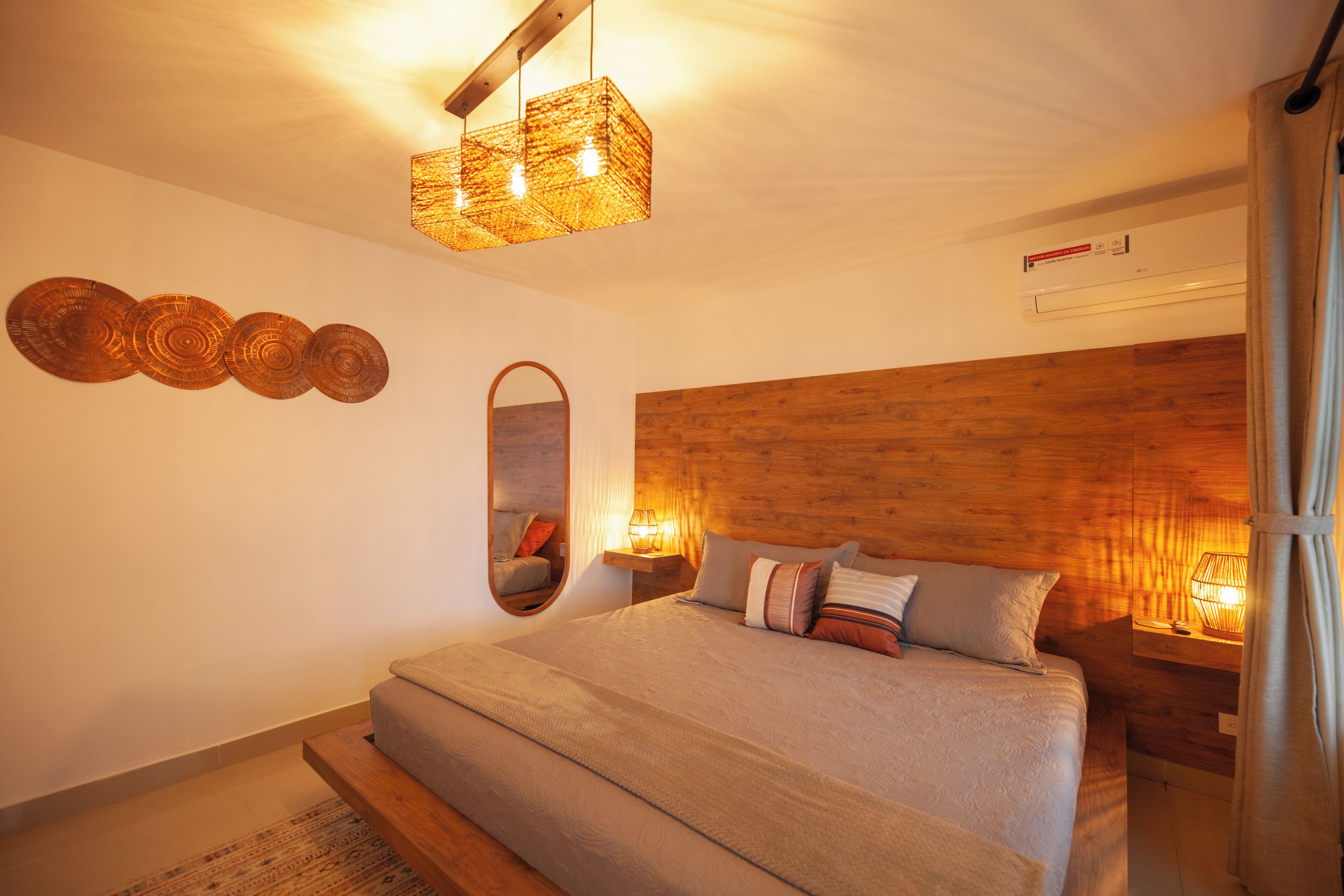 Ein Schlafzimmer mit einem großen Bett, einem Holzkopfstück, einem Spiegel und einer hängenden Leuchte.