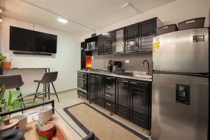 A modern kitchen with black cabinets, a stainless steel refrigerator, a flat-screen TV, and a dining area with two chairs and a table. - 2Bed-Jacuzzi unit in Astorga (Medellín)
