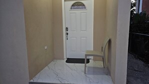A white door with a small window above it, a metal gate to the right, and a chair in front of the door. - Tandel Ocho Rios Apartment #1 (Ocho Rios)