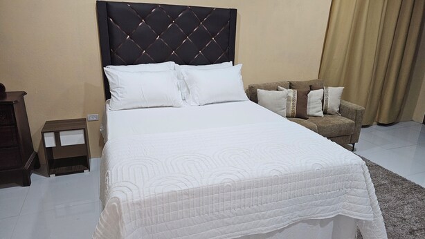 A neatly made bed with a tufted headboard, white bedding, and a small bedside table with a lamp. - Tandel Ocho Rios Apartment #1 (Ocho Rios)