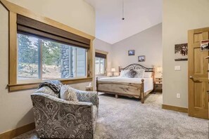 Un dormitorio con un ventanal grande, una cama, una silla y una puerta.