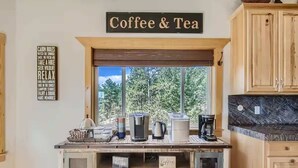 Une cuisine équipée d’un espace dédié au café et au thé, d’une fenêtre donnant sur la verdure et de meubles de rangement en bois.