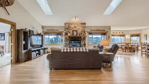 Un salon spacieux avec une cheminée en pierre, un plancher en bois et une grande fenêtre.
