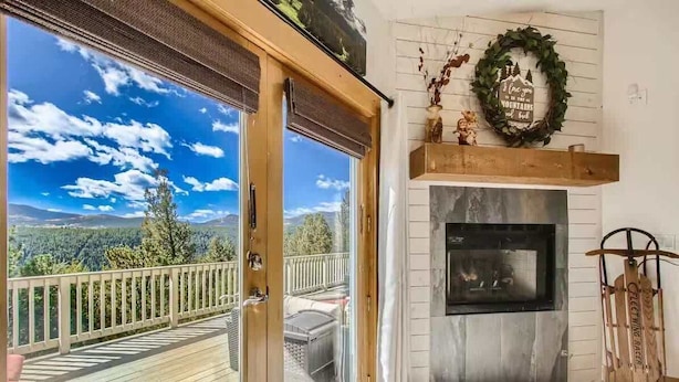Une pièce avec une cheminée, une vue sur les montagnes par une porte-fenêtre coulissante et une terrasse en bois.