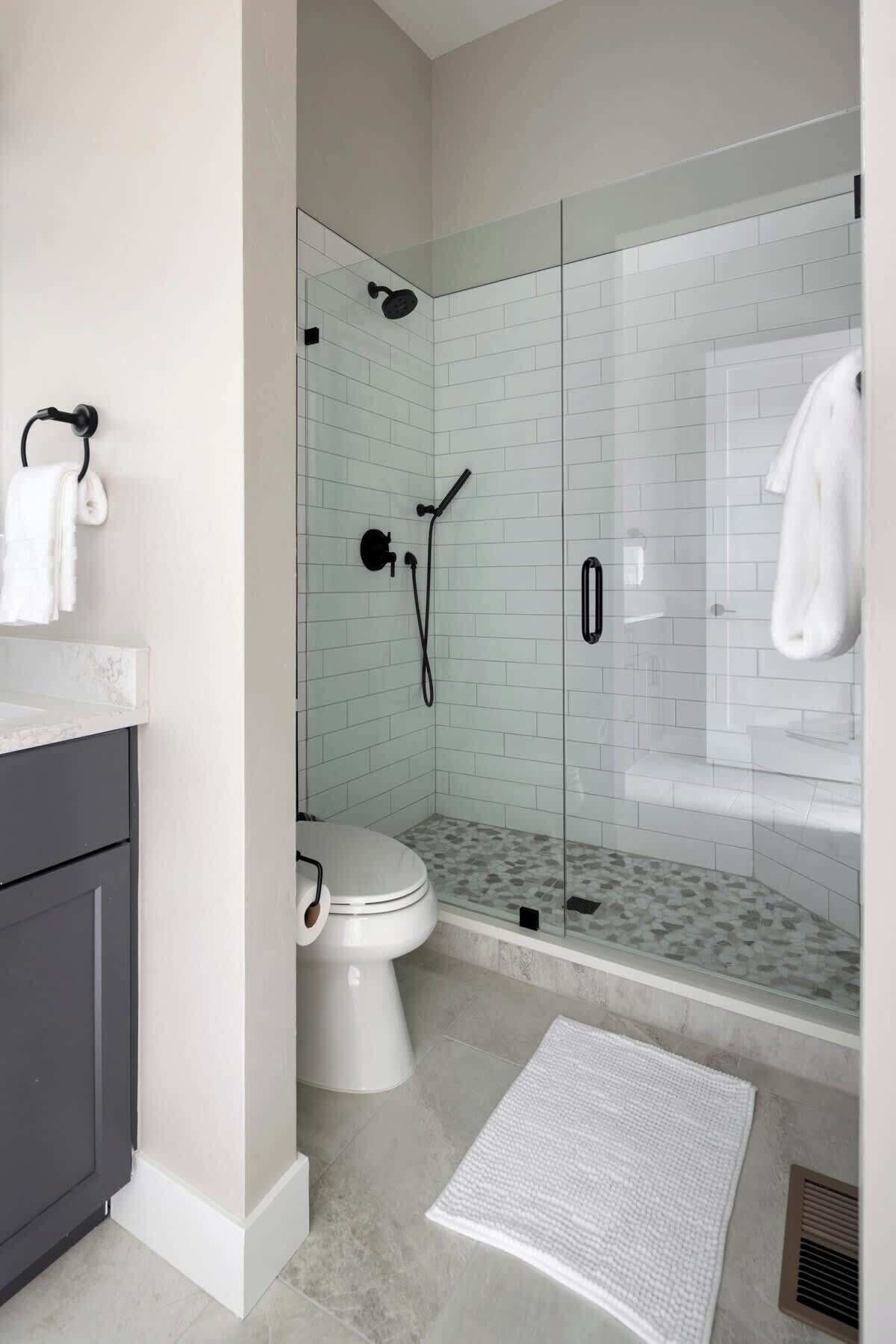 Un baño moderno con ducha acristalada, inodoro y tocador con toallero.