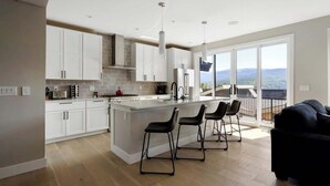 Une cuisine moderne avec des meubles blancs, un îlot central doté de tabourets et une grande fenêtre offrant une vue sur les montagnes.