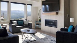 Un salon moderne avec un canapé, une table basse et une cheminée. De grandes fenêtres offrent une vue sur les montagnes.