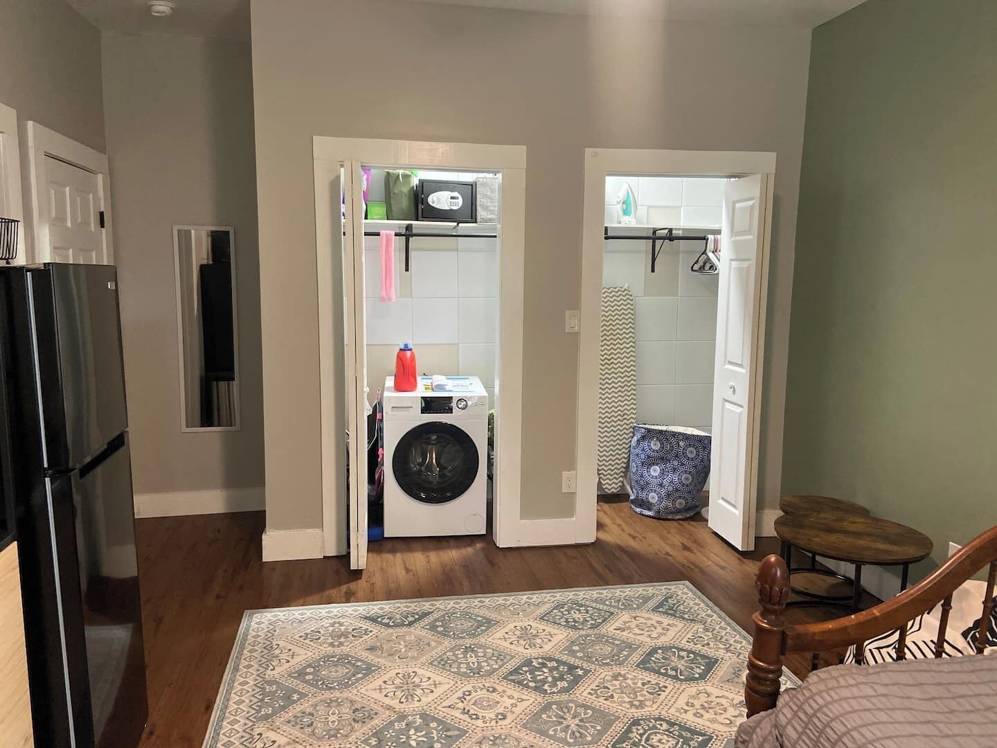 A compact kitchen with a refrigerator, washing machine, and a small dining area with a chair and table.