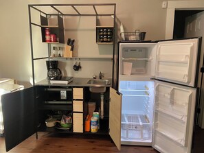Una cocina compacta con un refrigerador integrado, una cafetera y un lavamanos.