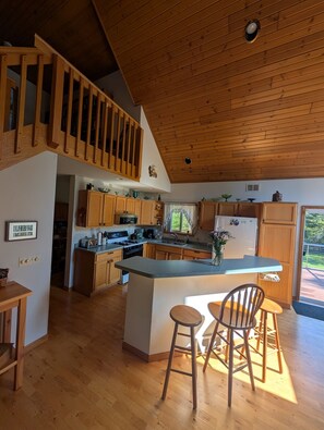 A spacious kitchen with wooden cabinets, a central island, and a high ceiling with exposed beams. - Spacious 3BR Lake Cabin – Fishing, Fire Pit & ATV/UTV Access (Tomahawk)
