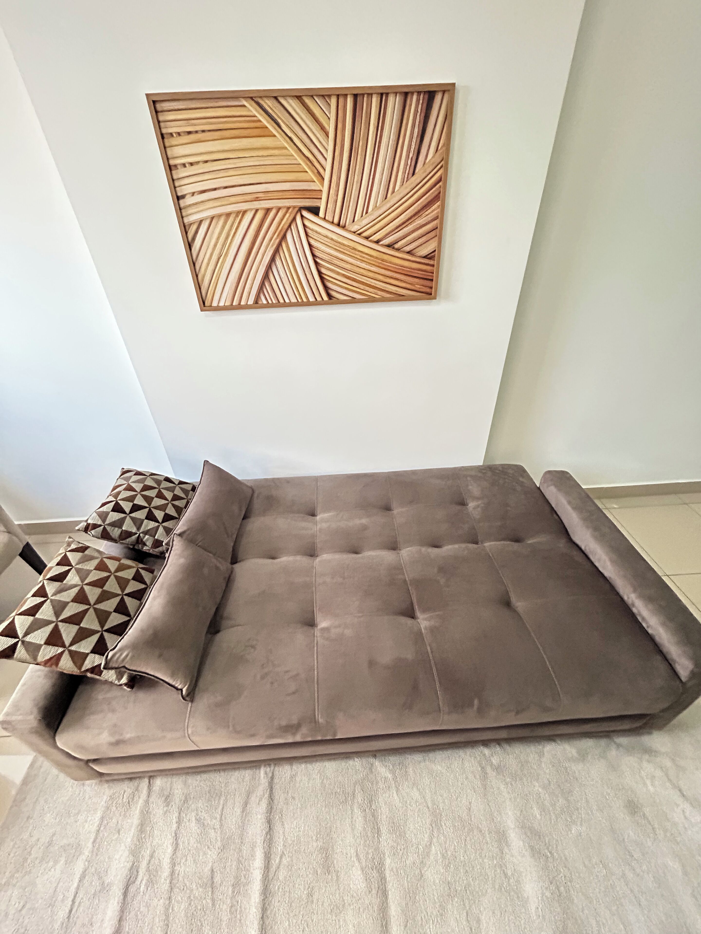 A modern living room with a large sofa, patterned cushions, and a geometric wall art piece.