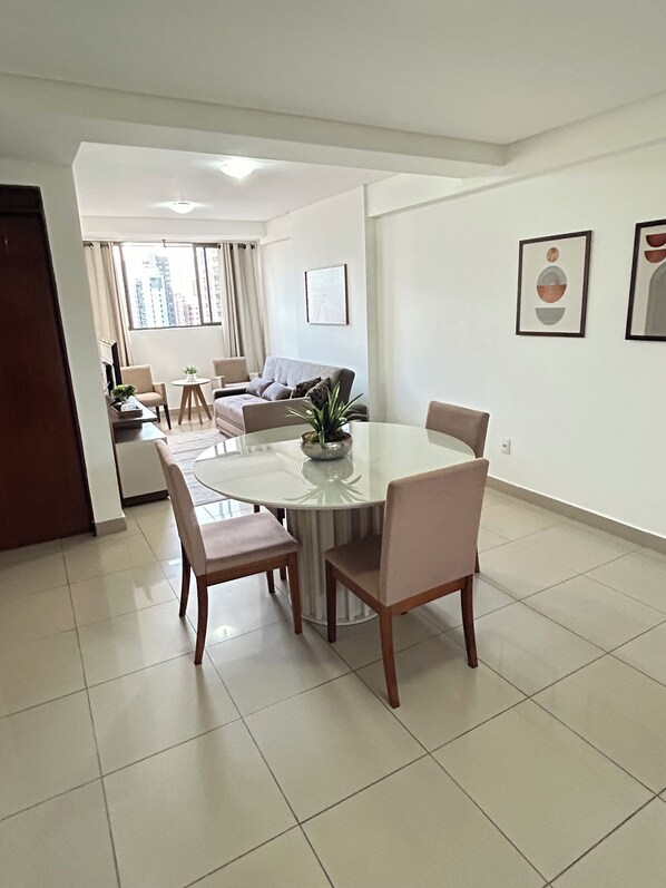 A modern living room with a dining area, featuring a round table and chairs, a sofa, and a coffee table. - Melhores Flats - Coração de Tambaú (João Pessoa)