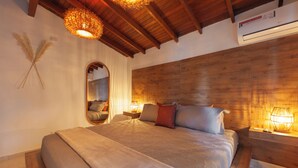 Ein Schlafzimmer mit einem hölzernen Kopfende, einem großen Bett mit einer beige farbenen Decke, zwei Nachttischlampen und einer Wandklimaanlage.