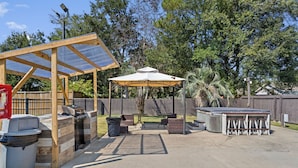 Une terrasse extérieure dotée d’un espace barbecue couvert, d’une table avec des chaises et d’une poubelle.