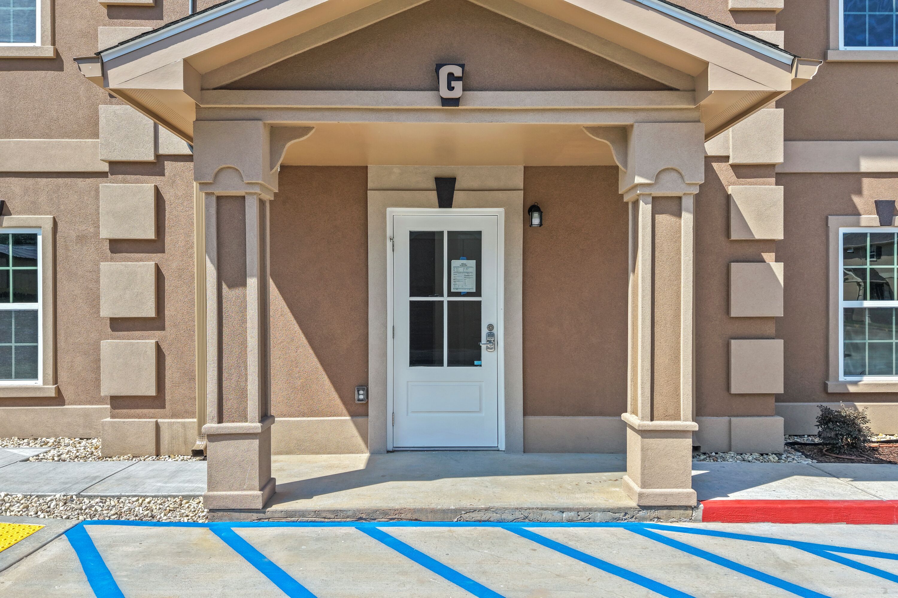A building entrance with a white door, columns, and a 'G' sign above.
