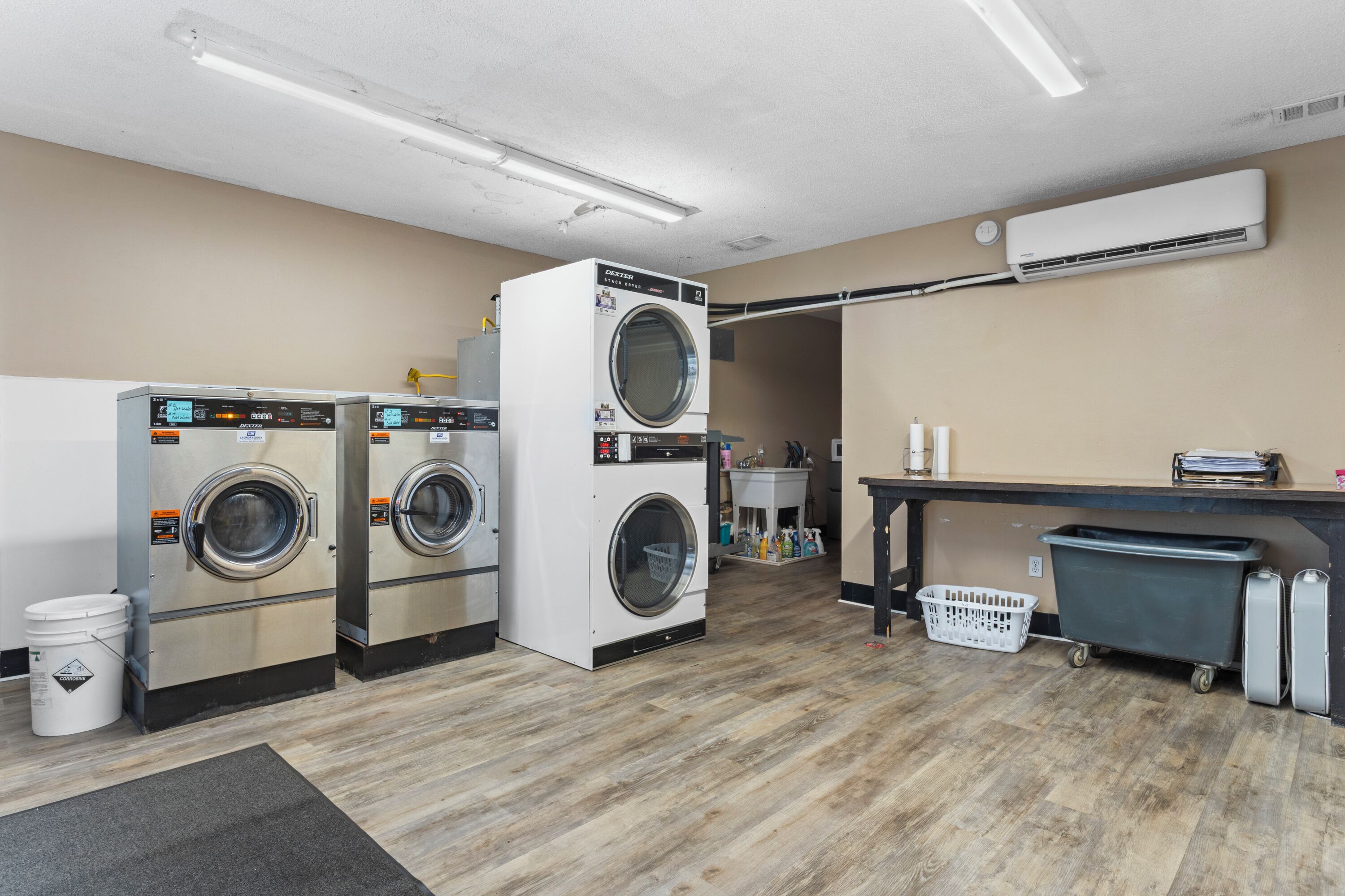A laundry facility with multiple washing machines, a utility cart, and a trash bin.
