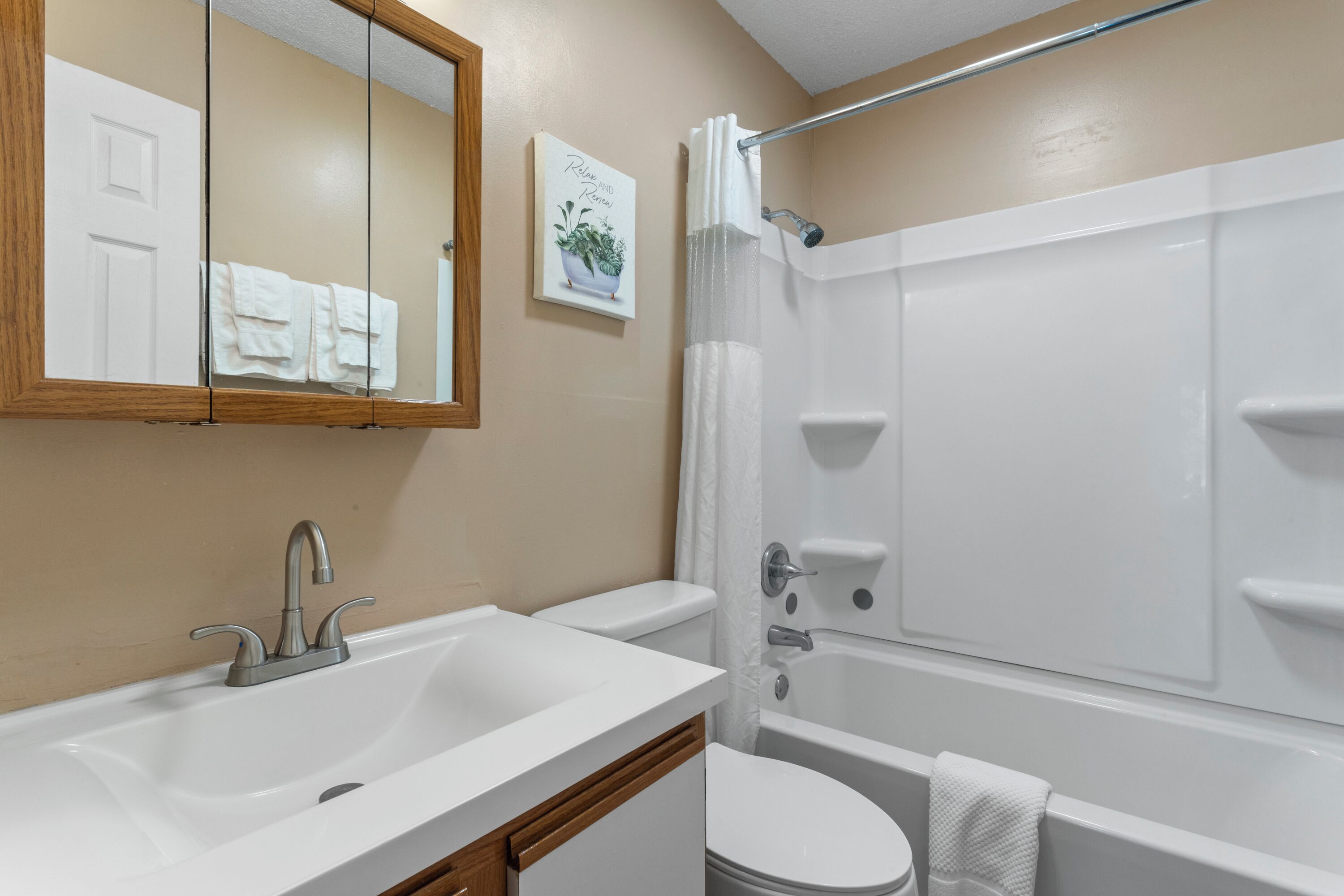 A bathroom with a white sink, toilet, and bathtub. There is a mirror above the sink and a towel hanging on the wall.