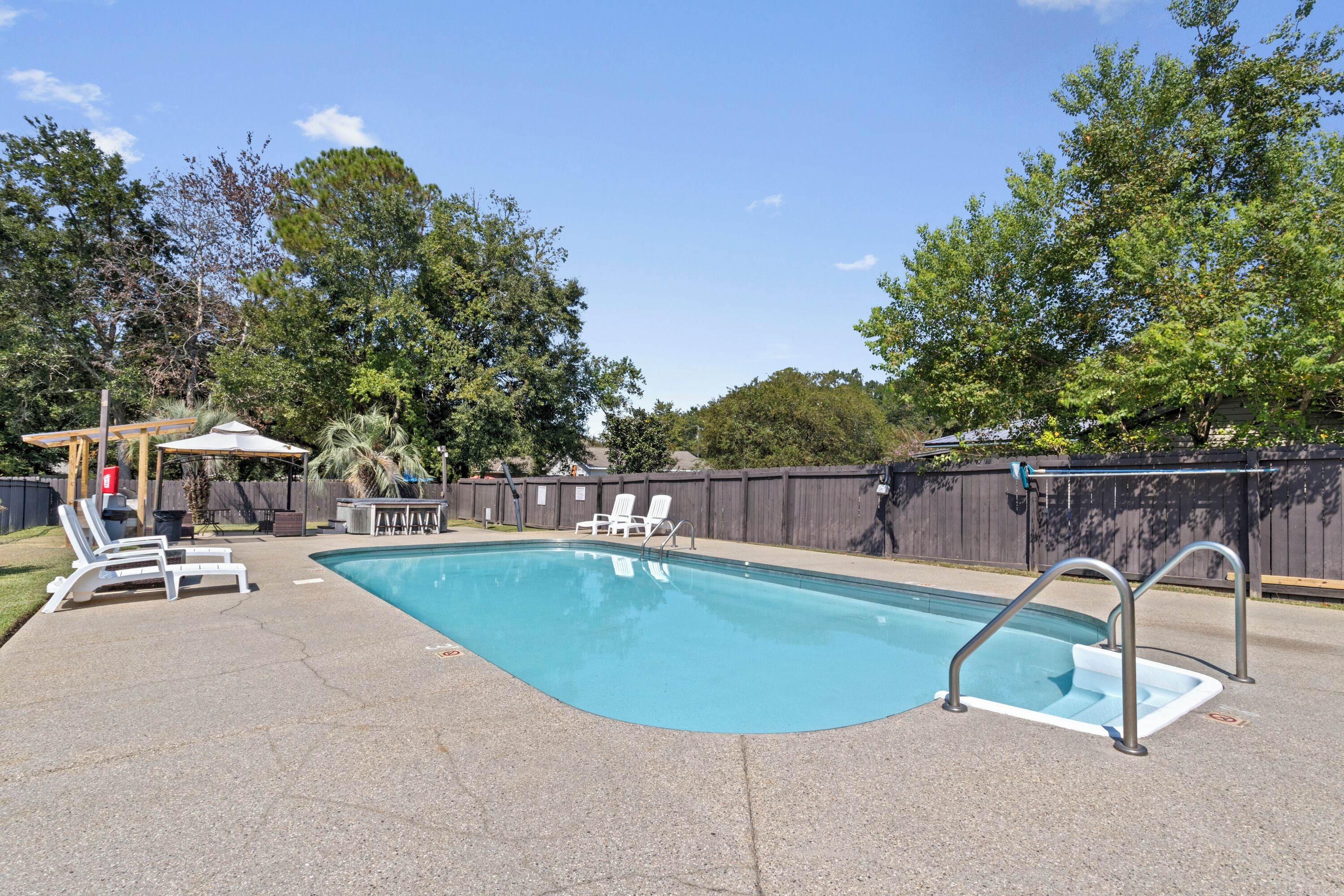 Una piscina rectangular con una escalera incorporada y dos sillas reclinables a un lado.