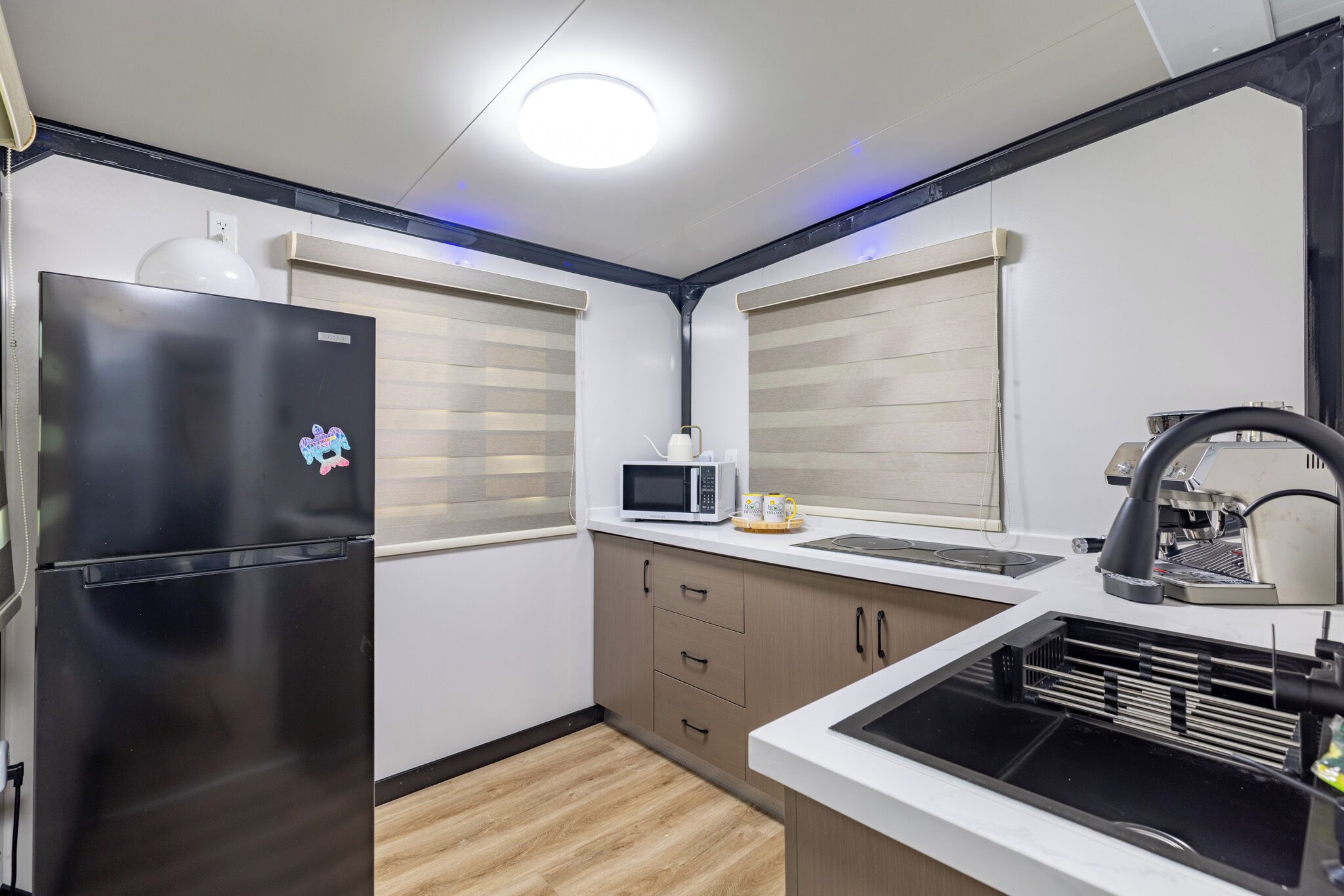 Une cuisine compacte avec un réfrigérateur noir, un four à micro-ondes et un évier doté d’un robinet noir.
