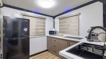 Une cuisine compacte avec un réfrigérateur noir, un four à micro-ondes et un évier doté d’un robinet noir.