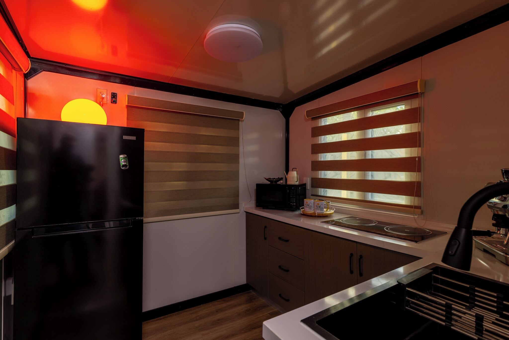 A compact kitchen with a black refrigerator, wooden cabinets, a microwave, and a coffee machine.