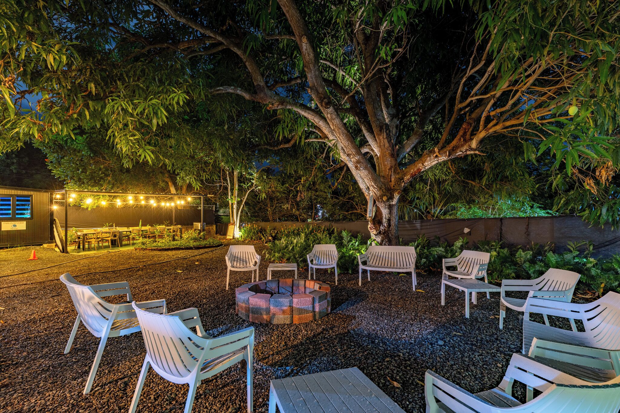 An outdoor seating area with chairs and tables, surrounded by trees and a fire pit.