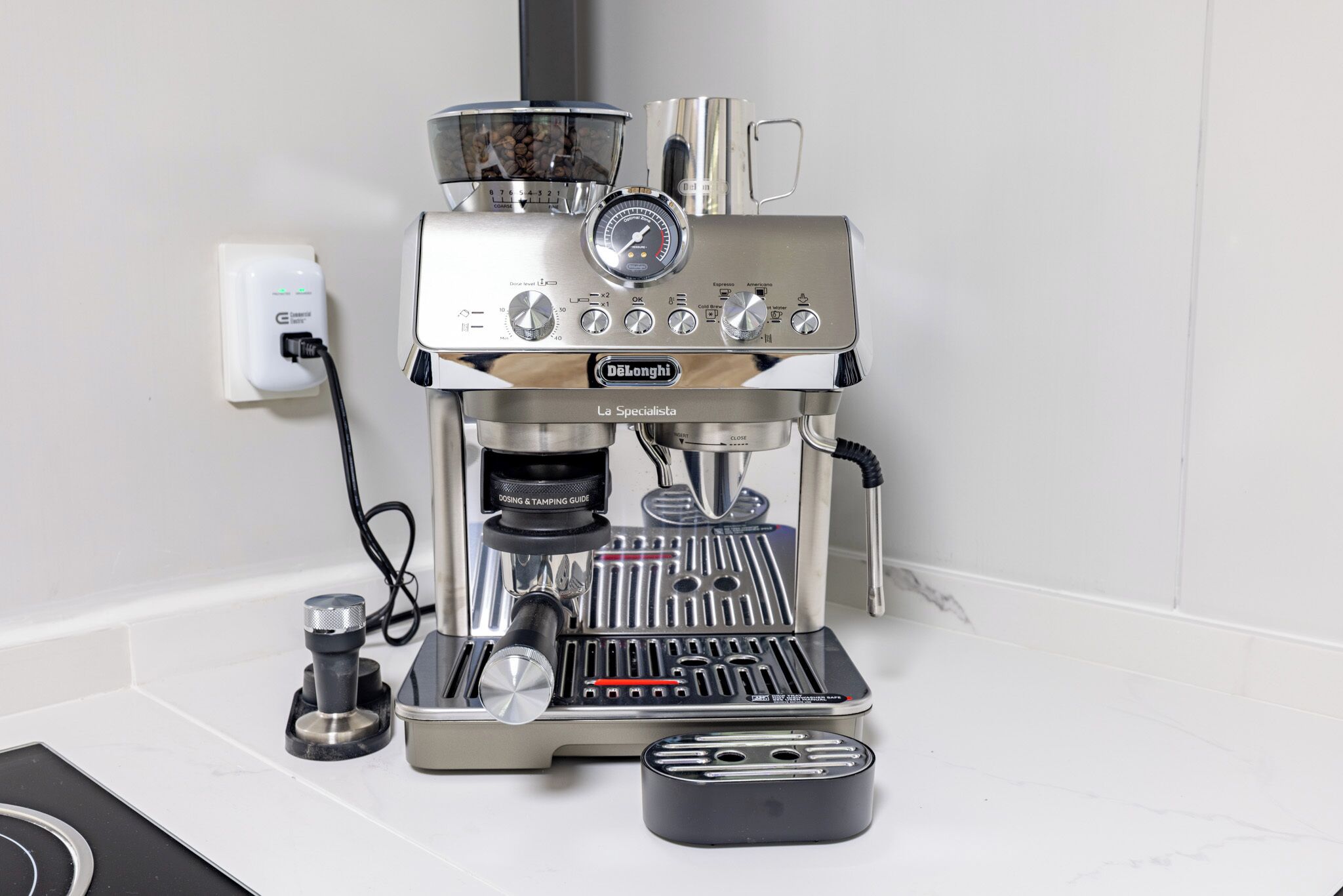 Una màquina d'espresso De'Longhi La Specialista amb un manòmetre digital, un portafiltre i un traçador sobre un taulell blanc.