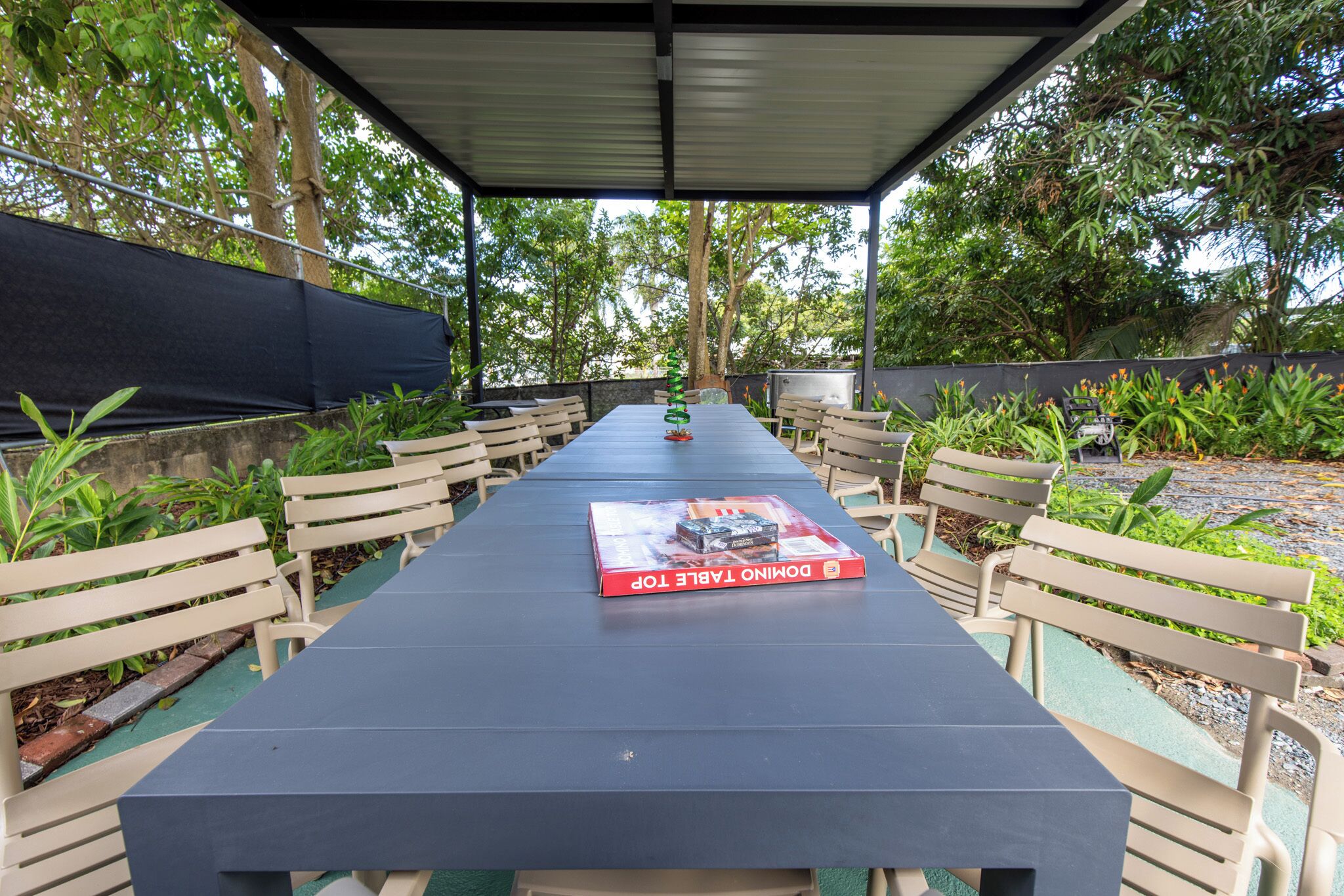 An outdoor covered dining area with a long table, benches, and a book titled "Domino Table Top."