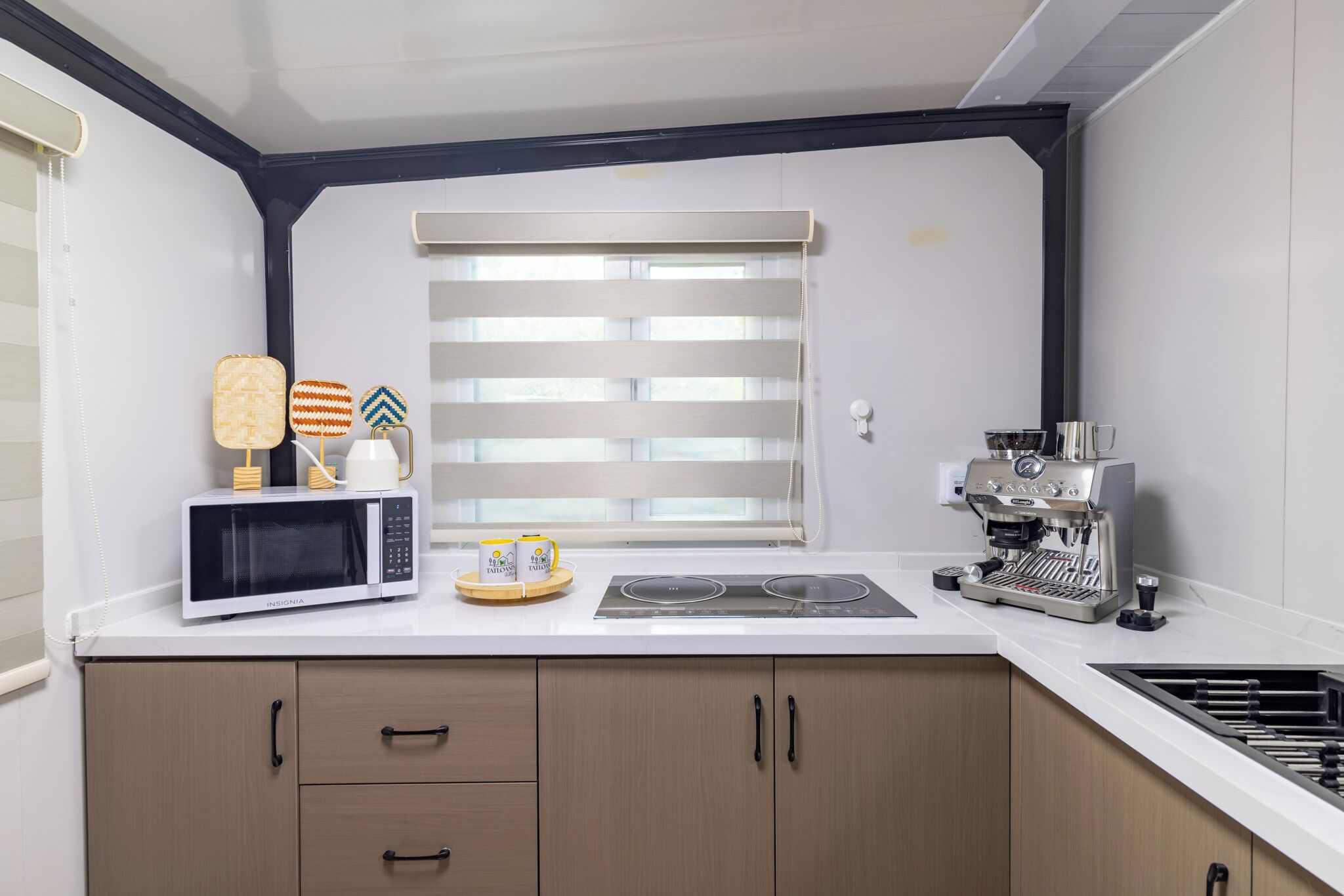 A modern kitchen with a microwave, coffee machine, and a window with blinds.