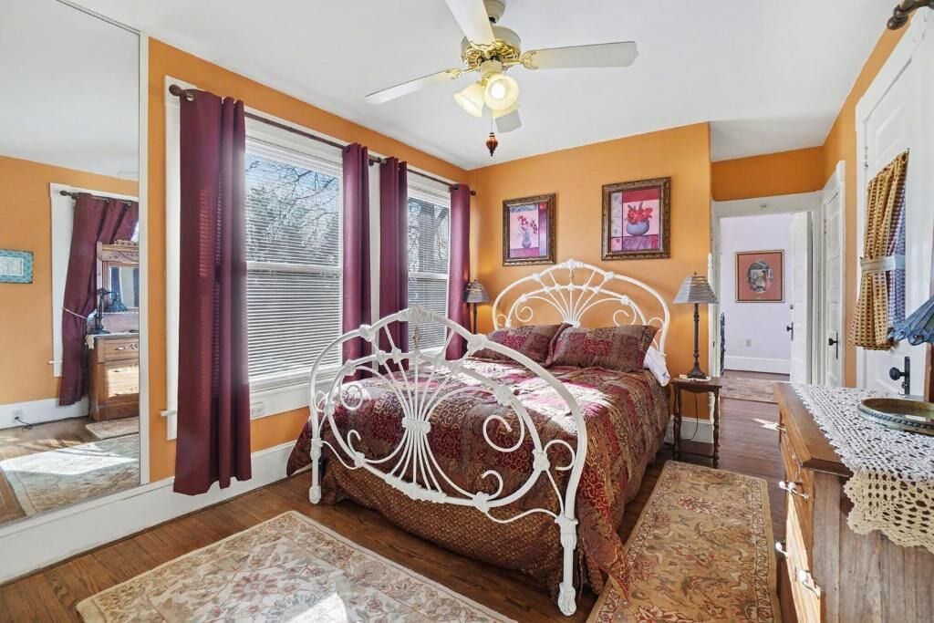 A bedroom with a white ornate bed, a ceiling fan, and a large window with purple curtains.