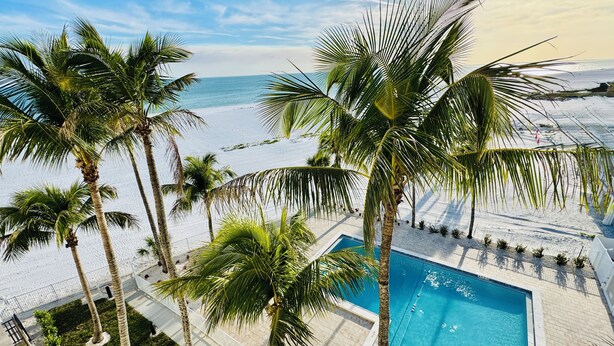 Udsigt over poolen med palmer, en klar himmel og en strand i baggrunden.