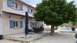 Un edificio a due piani con persiane blu, un patio con tavolo e sedie e una piscina sullo sfondo.