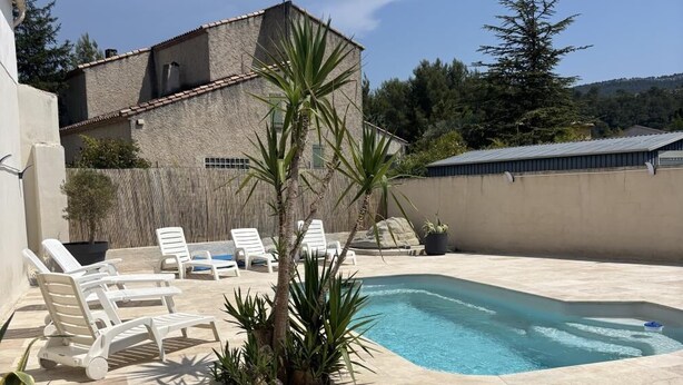 Una piscina con lettini, una piccola palma e un edificio sullo sfondo.