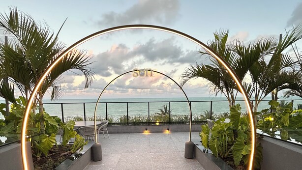 An outdoor pathway with a metal archway and illuminated lights, leading to a view of the sea.