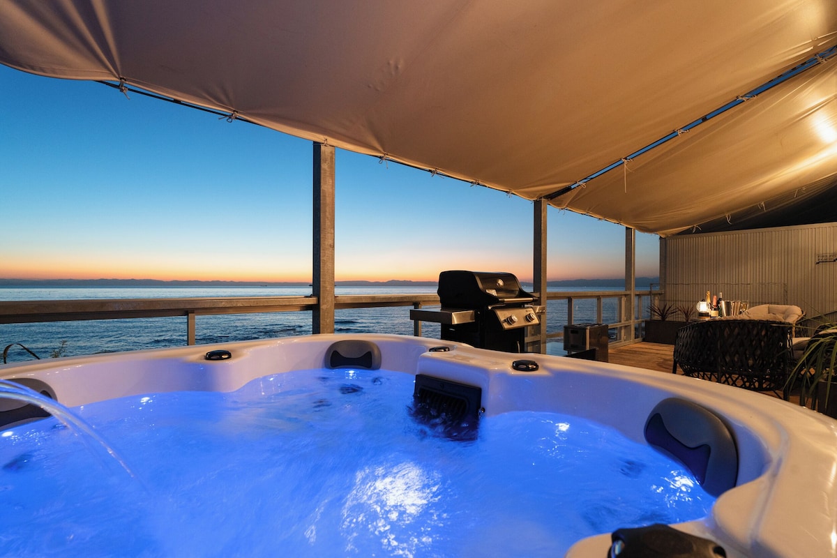 A hot tub with a sunset view, a grill, and outdoor furniture.