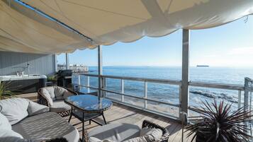 A covered outdoor seating area with wicker furniture, a table, and a view of the sea.