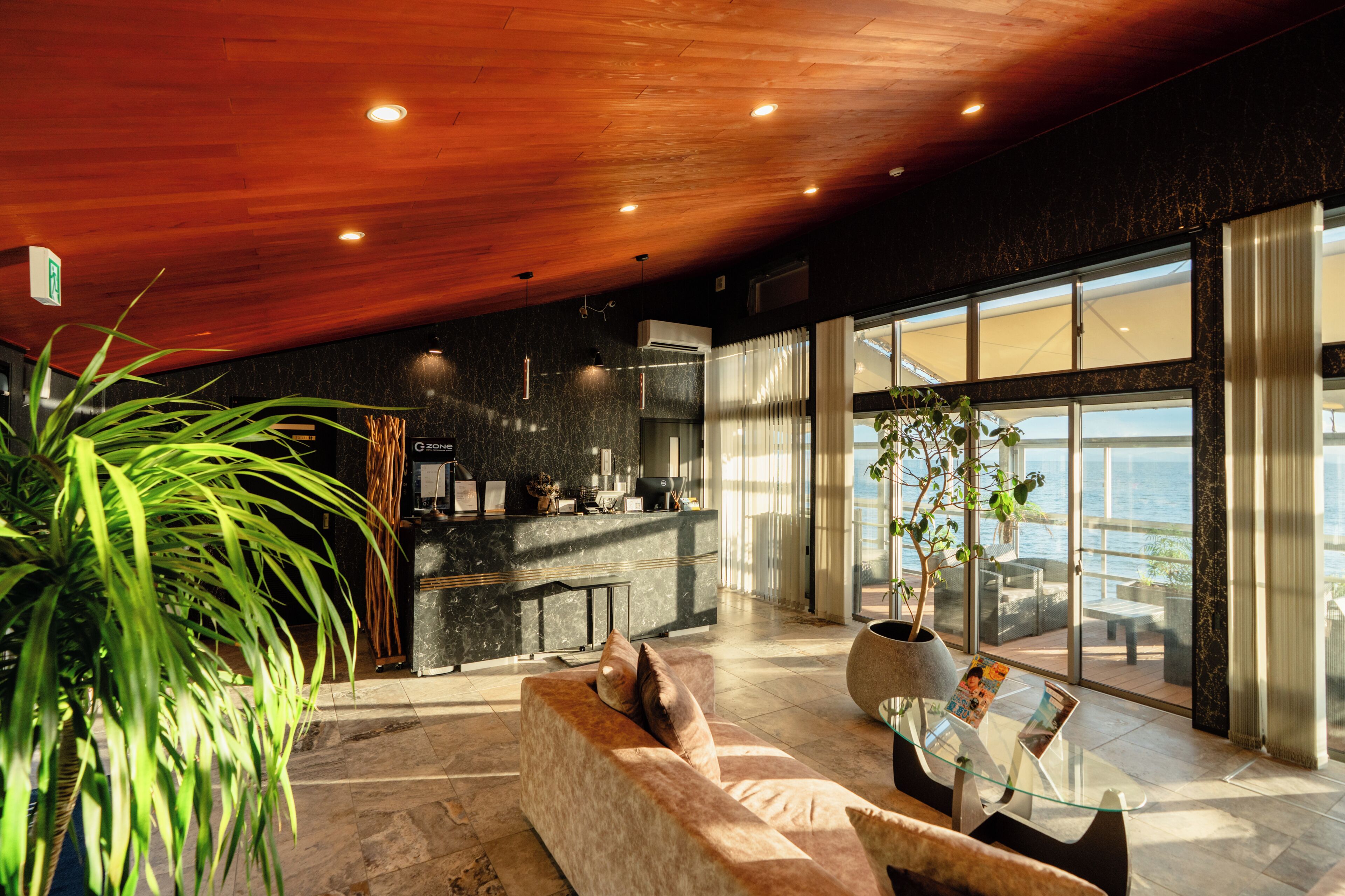A modern interior with a wooden ceiling, a sofa, a coffee table, and a view of the sea through large windows.