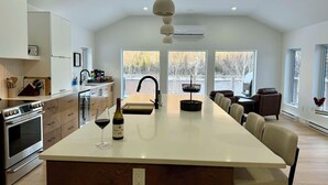 Une cuisine moderne avec un îlot central, un coin repas avec des chaises et de grandes fenêtres offrant une vue sur un lac.