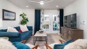 A living room with a blue sofa, a coffee table, a TV, and a ceiling fan. - Modern Upgrades & Comfort (Oxford)