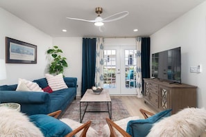 Ein Wohnzimmer mit einem blauen Sofa, einem Couchtisch, einem Fernseher und einem Deckenventilator.