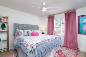A bedroom with a bed, a ceiling fan, a window with curtains, a wall-mounted shelf, and a painting.