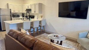 Una cucina moderna con mobili bianchi, una TV a schermo piatto, un divano in pelle marrone e un piccolo tavolo rotondo.