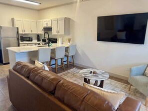 A modern kitchen with white cabinets, a flat-screen TV, a brown leather sofa, and a small round table. - Oxford Charm (Oxford)