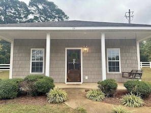 A single-story house with a covered porch, a front door, and a swing bench. - Oxford Charm (Oxford)