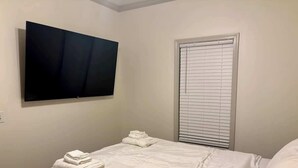 Una camera da letto con un letto, una televisione a parete e una finestra con persiane.