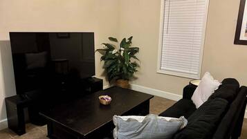 A living room with a dark wooden coffee table, a black sofa, a television, and a potted plant.