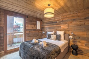 A wooden-paneled bedroom with a bed, a fluffy rug, and a nightstand. - Appartement Jorat - Welkeys (Megève)