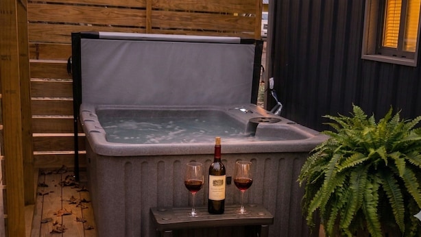 A hot tub with a wooden deck and a table with a bottle of wine and two glasses.