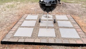 A barbecue grill on a paved patio with a camper in the background.