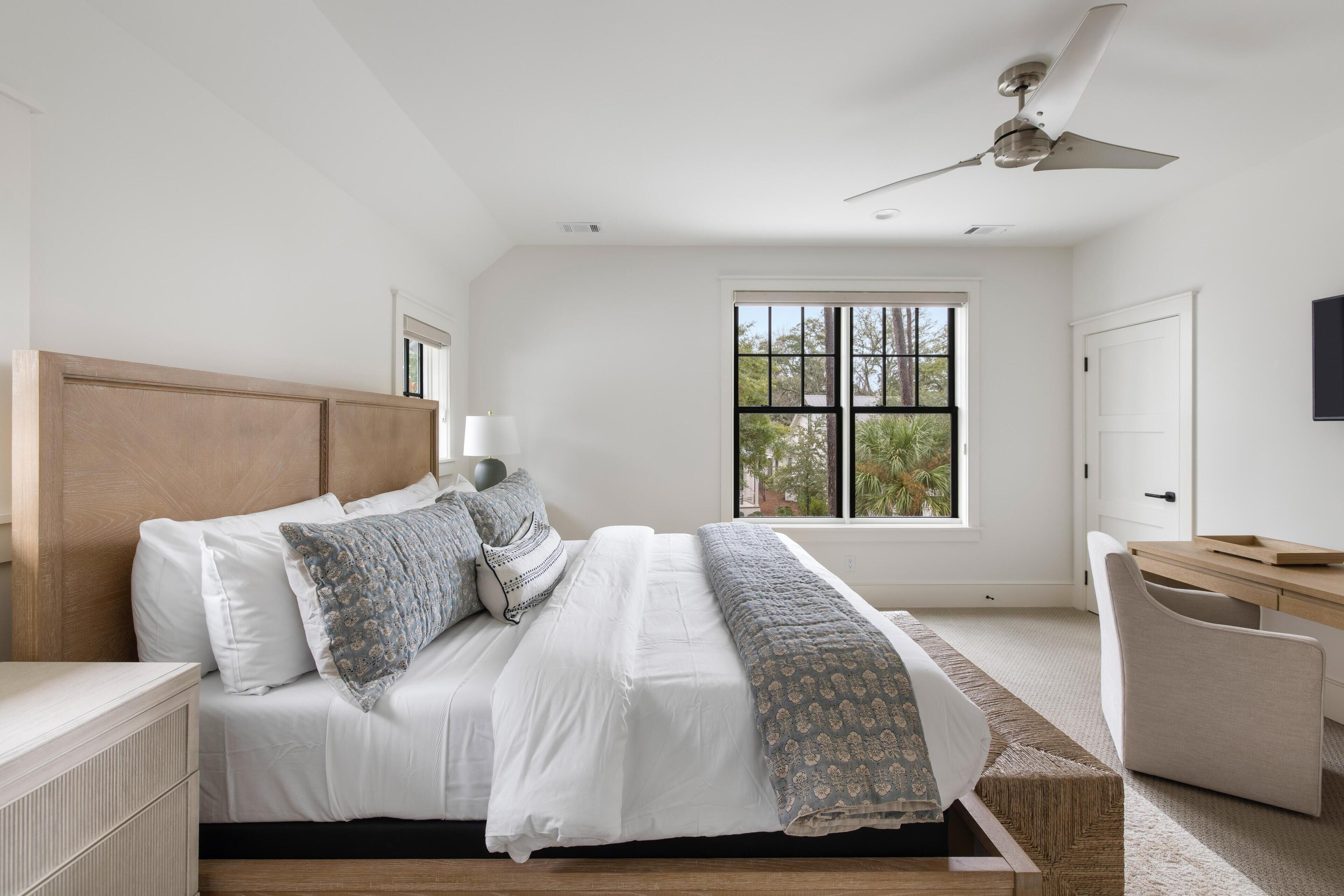 A bedroom with a bed, bedside table, lamp, window, and desk.